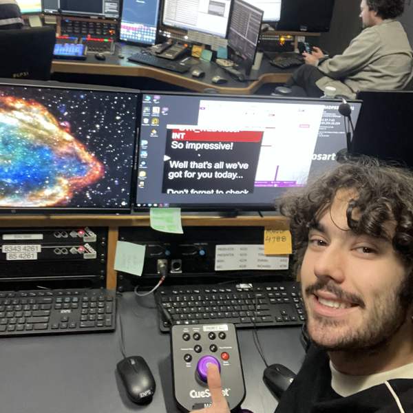 Xander at the gallery desk in a broadcast control room, hand on the autocue control
