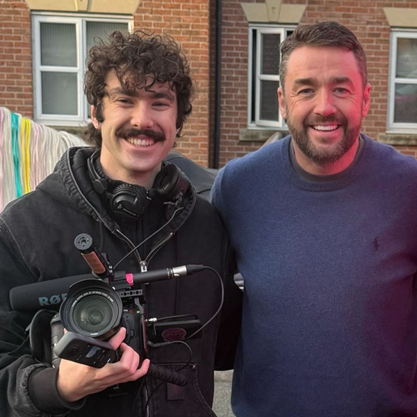 Xander with a shoulder-rig camera standing beside Jason Manford