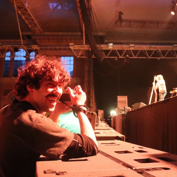 Xander grinning at a mixing desk with Iggy Pop on stage behind him