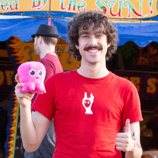 Xander at a festival holding a pink Octopus plush toy, thumb up