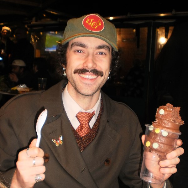 Xander in a tweed coat and cap holding an ice cream and a spoon